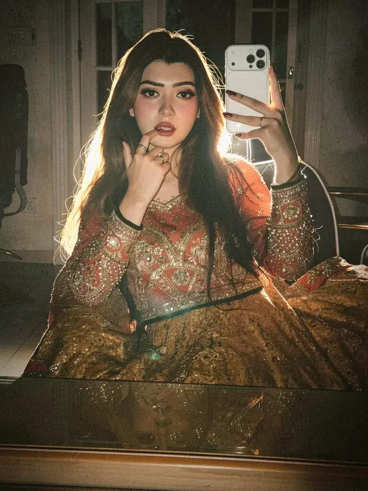 A Close-Up Photo Of A Young Woman With Long Brown Hair, Adorned In A Stunning Red And Gold Dress, Taking A Selfie In Fro