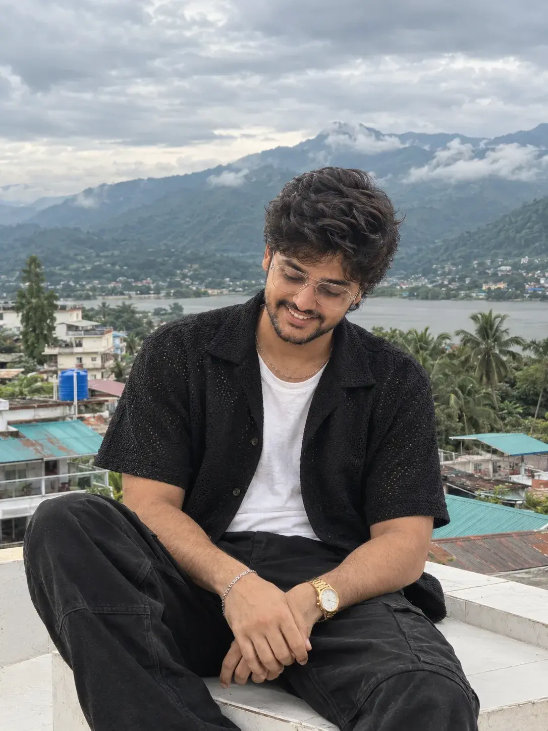 A Relaxed Rooftop Portrait With A Warm, Genuine Smile, Textured Black Layers, And A Misty Mountain.