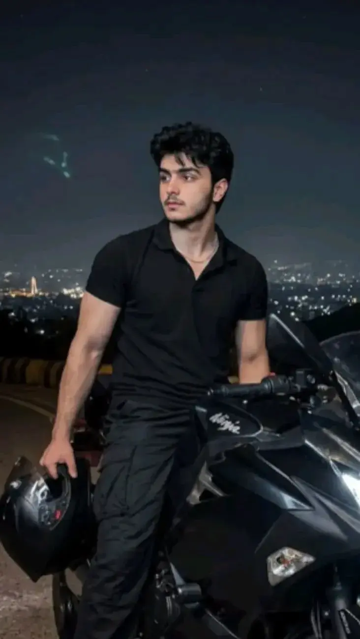 A Young Man Standing Confidently On A Sleek Black Motorcycle