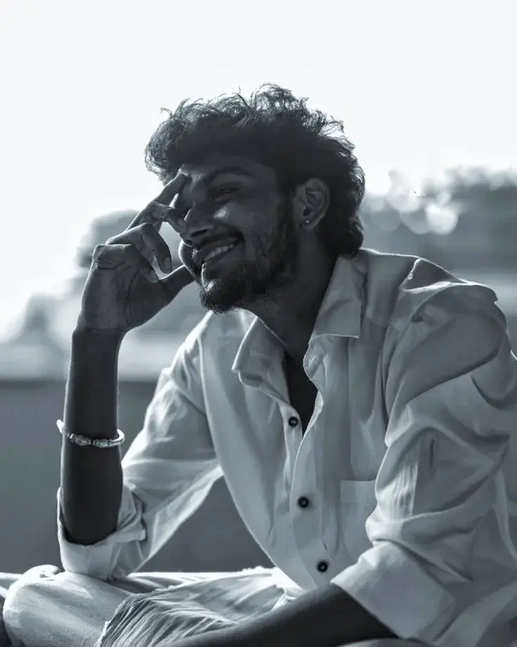 Candid Black-And-White Contemplative Portrait Of Smiling Young South Asian Man With Curly Hair And Silver Kada In White
