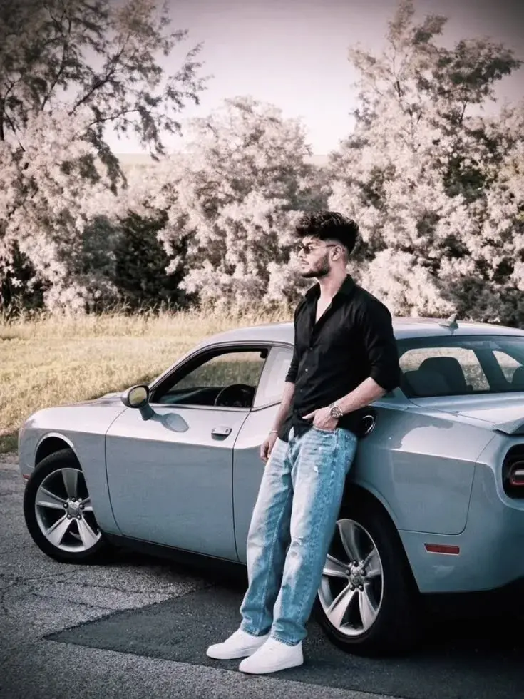 Candid Countryside Roadside Portrait Of Young South Asian Man Leaning Against Silver Dodge Challenger In Black Shirt And
