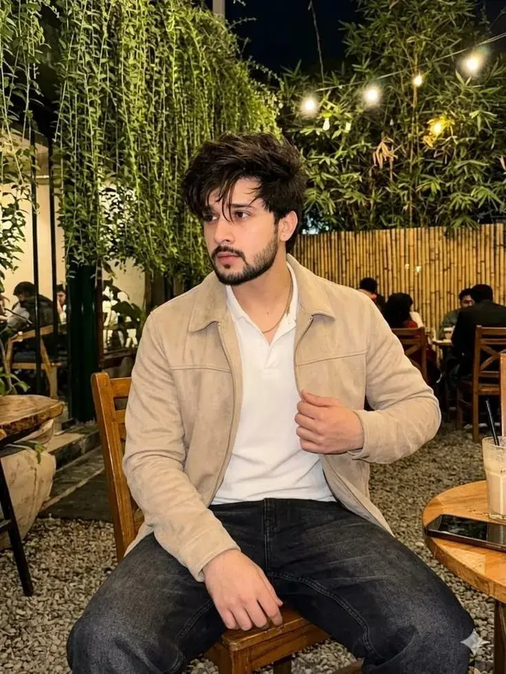 Candid Evening Cafe Patio Portrait Of Handsome Young South Asian Man In Suede Jacket And Polo Shirt Leaning Forward