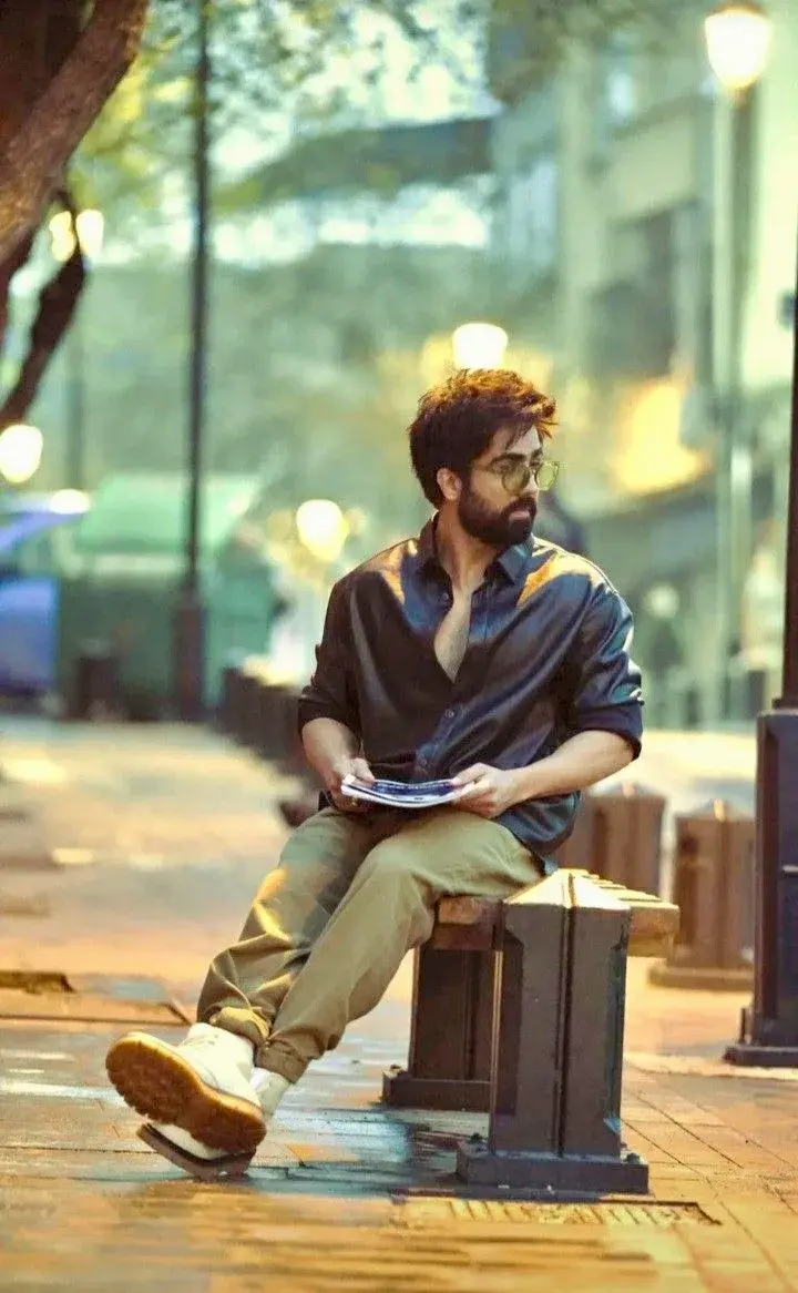 Candid Evening City Street Portrait Of Young South Asian Man With Beard And Sunglasses Seated On Wooden Bench