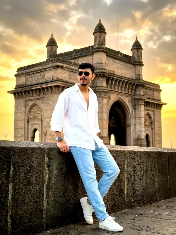 Candid Full-Length Golden Hour Portrait Of Young South Asian Man Leaning On Seafront Wall In Front Of Gateway Of India M