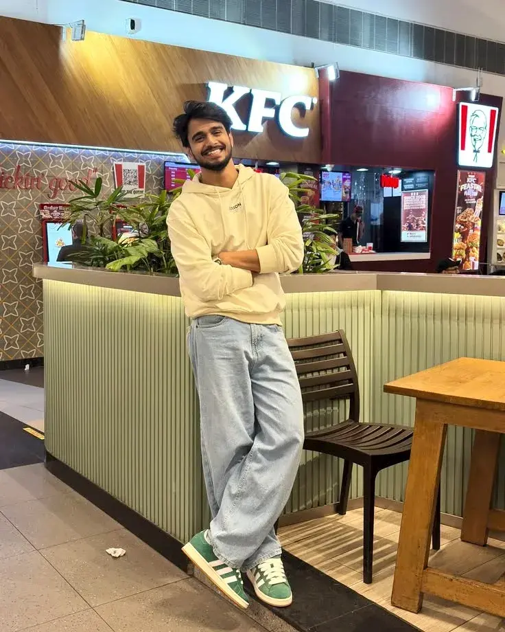 Candid Full-Length Indoor Food Court Portrait Of Smiling Young South Asian Man Leaning On Fluted Counter