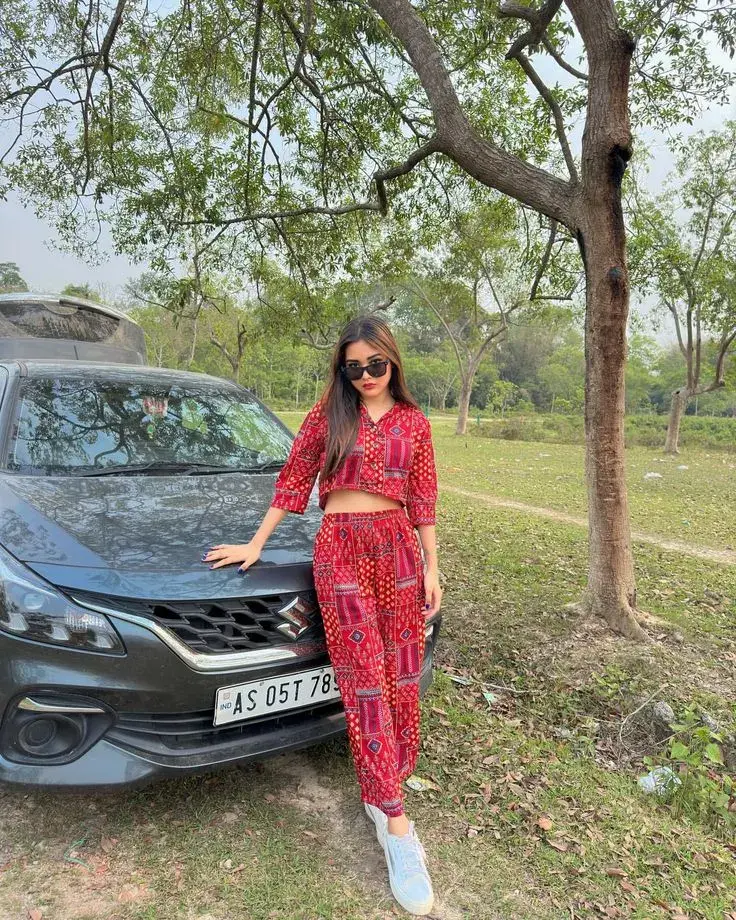 Candid Full-Length Outdoor Portrait Of Young South Asian Woman In Red Printed Co-Ord Set Leaning Against Car Hood
