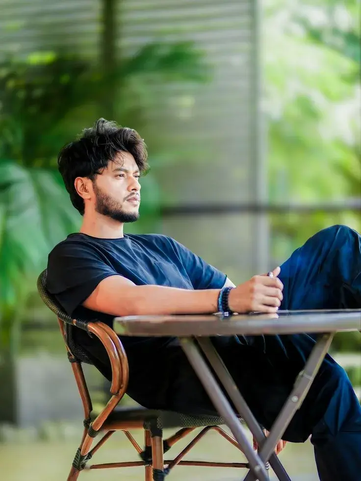 Candid Garden Cafe Portrait Of Pensive Young South Asian Man In Black T-Shirt Lounging At Outdoor Bistro Table