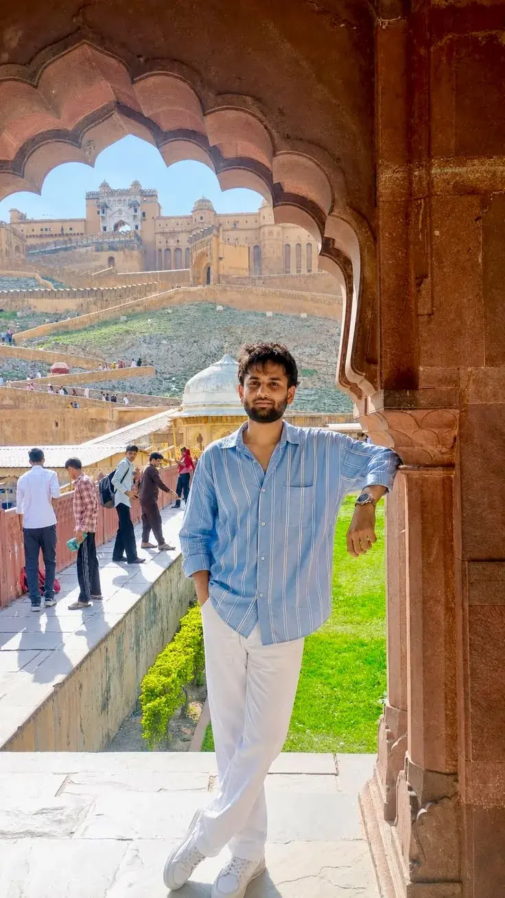 Candid Heritage Fort Portrait Of Young South Asian Man In Light Blue Striped Shirt Leaning On Ornate Sandstone Arch