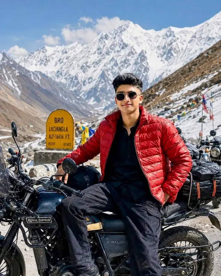Candid Himalayan Mountain Pass Portrait Of Smiling Young South Asian Man In Red Puffer Jacket Sitting On Royal Enfield M