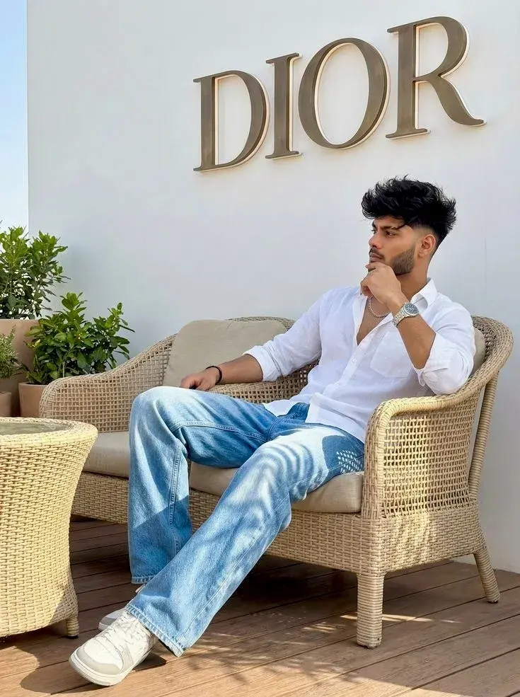 Candid Luxury Rooftop Terrace Portrait Of Handsome Young South Asian Man In White Linen Shirt Lounging On Wicker Sofa