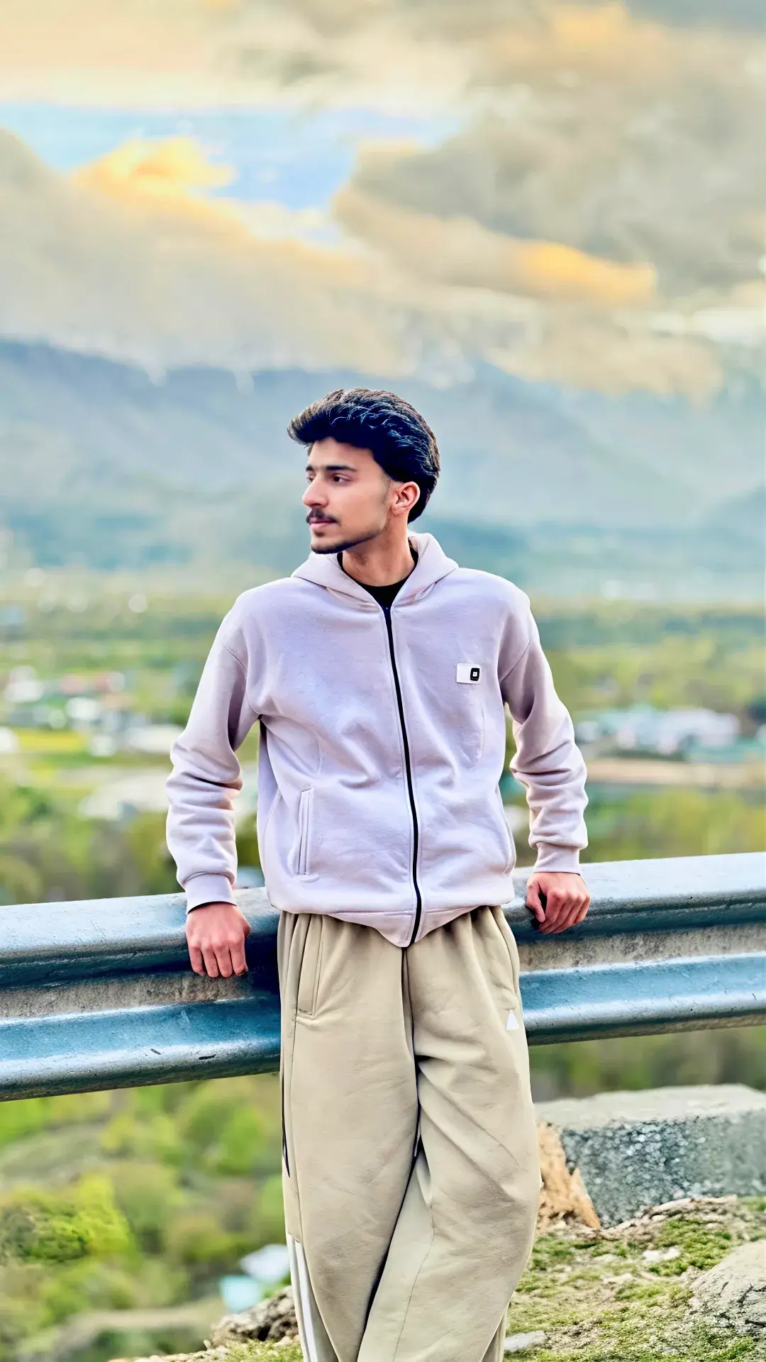 Candid Mountain Highway Overlook Portrait Of Handsome Young South Asian Man In Lilac Fleece Zip Hoodie Leaning On Guardr