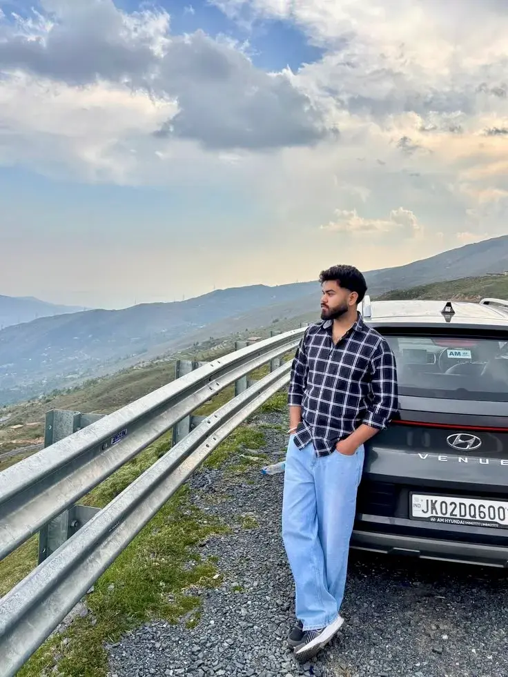 Candid Mountain Highway Overlook Portrait Of Handsome Young South Asian Man Leaning On Grey Suv With Metal Guardrail