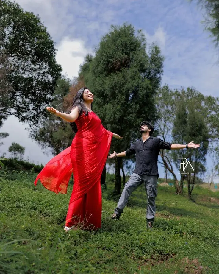 Candid Mountain Meadow Pre-Wedding Portrait Of Joyful Young South Asian Couple With Outstretched Arms In Red Saree And B