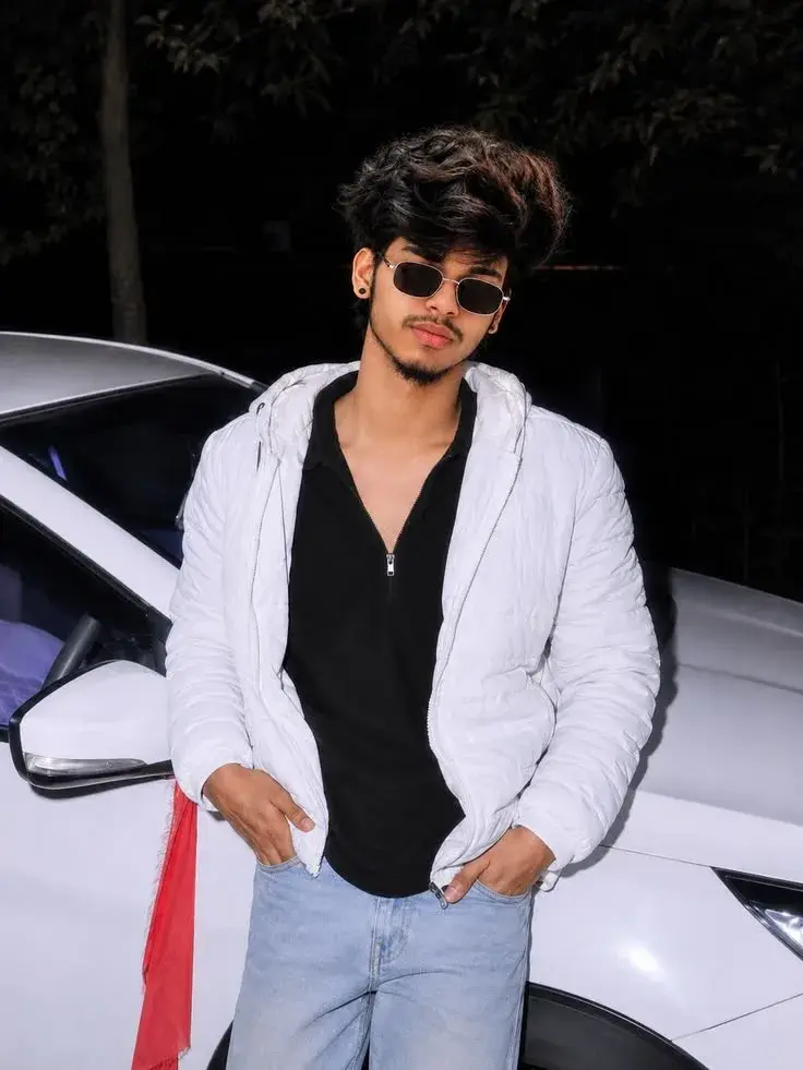 Candid Night Flash Portrait Of Young South Asian Man Leaning On White Car In White Puffer Jacket And Retro Sunglasses