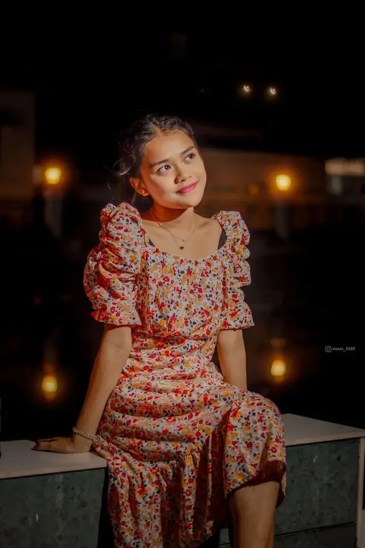 Candid Night Promenade Portrait Of Smiling Young South Asian Woman In Floral Puff-Sleeve Dress Seated On Low Wall