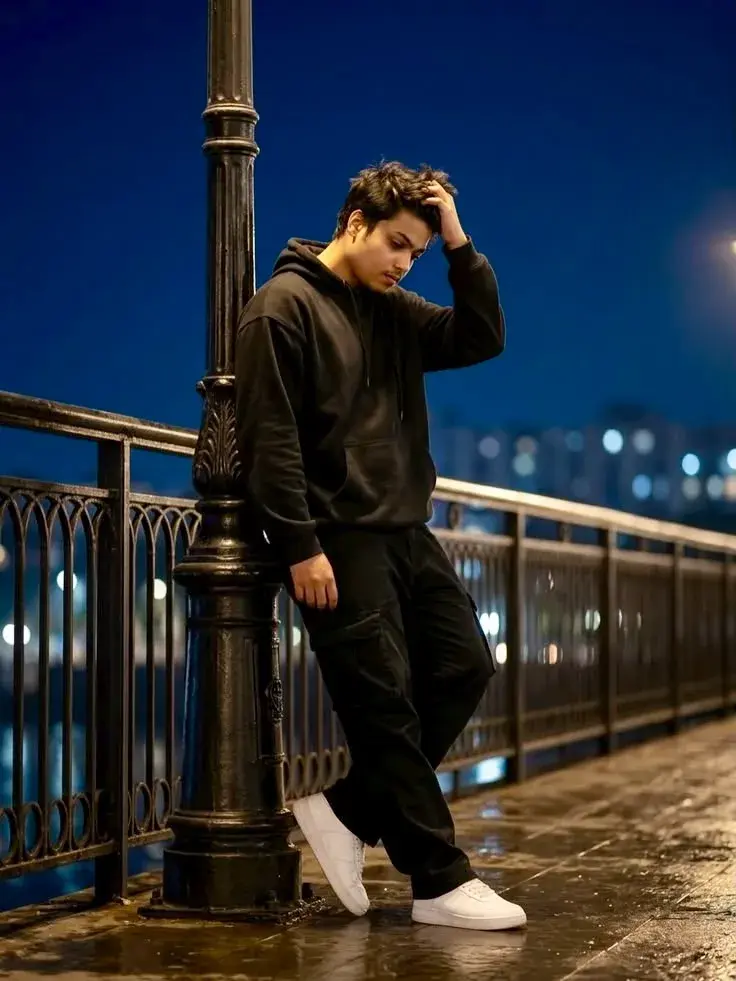 Candid Night Promenade Portrait Of Young South Asian Man In Black Hoodie Leaning Against Vintage Streetlamp Post