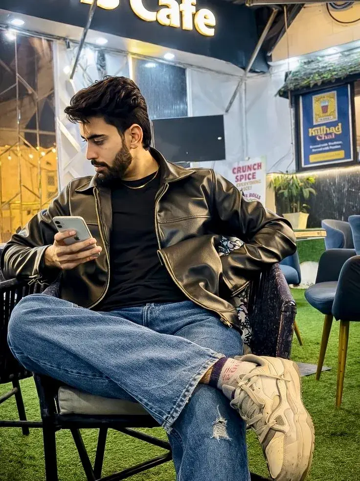Candid Outdoor Cafe Night Portrait Of Handsome Young South Asian Man In Brown Leather Jacket With Smartphone