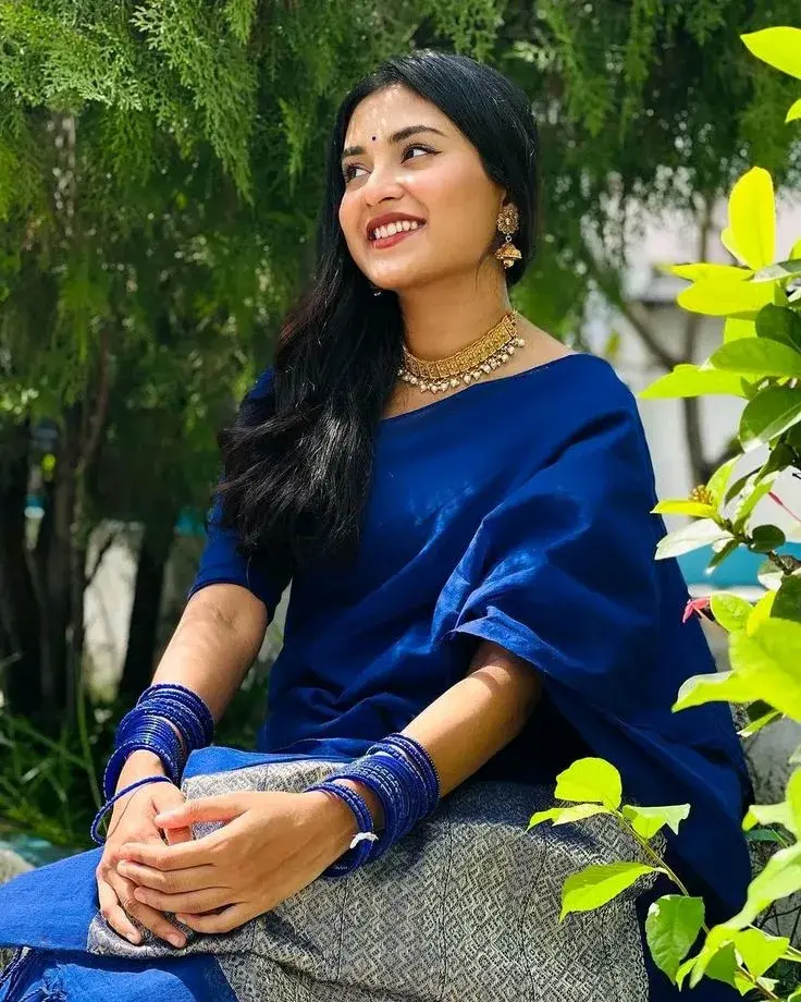 Candid Outdoor Garden Portrait Of Smiling Young South Asian Woman In Royal Blue Saree And Traditional Gold Jewelry