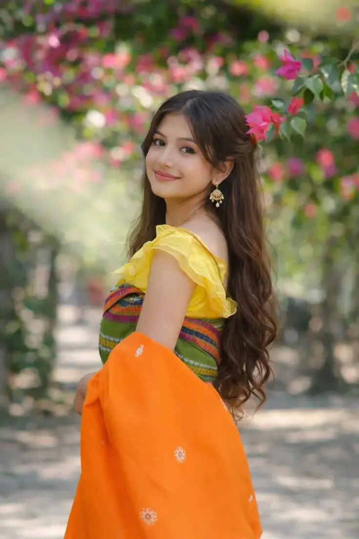 Candid Outdoor Garden Portrait Of Smiling Young South Asian Woman In Traditional Dokhna And Yellow Blouse Under Blooming