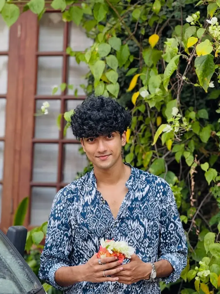 Candid Outdoor Garden Portrait Of Young South Asian Man In Blue Ikat Shirt Holding Small Bouquet