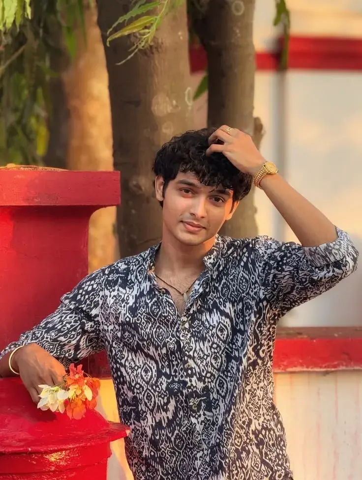 Candid Outdoor Golden Hour Portrait Of Young South Asian Man In Ikat Shirt Holding Flowers By Red Pillar