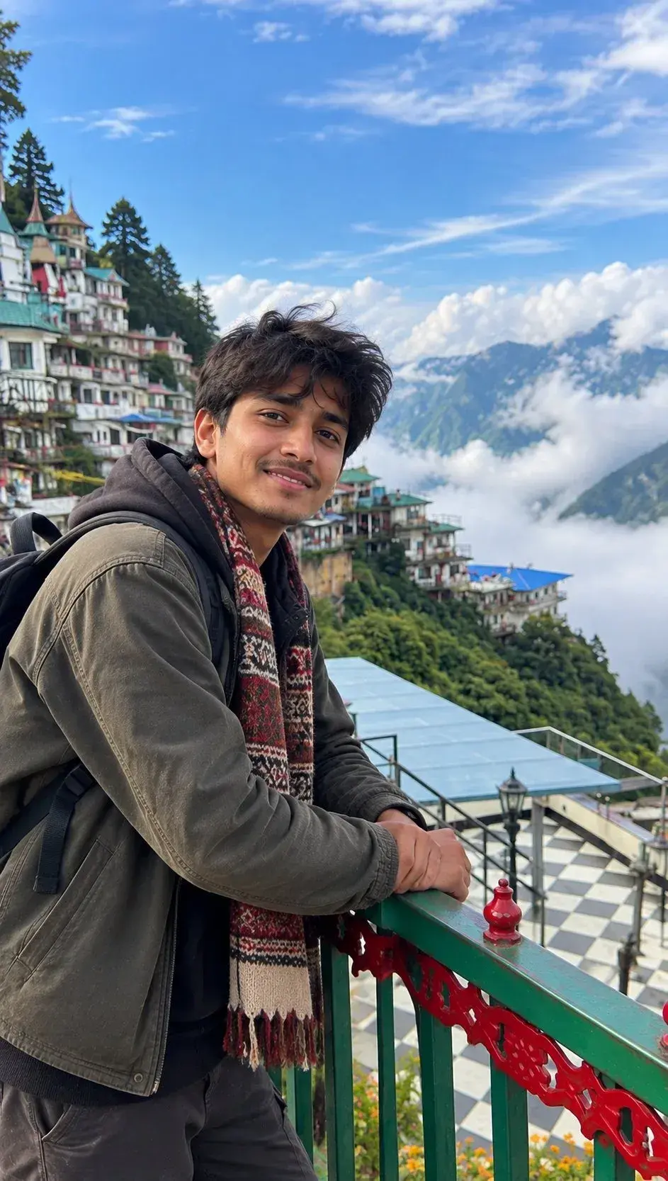 Candid Outdoor Mountain Overlook Portrait Of Smiling Young South Asian Man Leaning On Balcony Above Sea Of Clouds