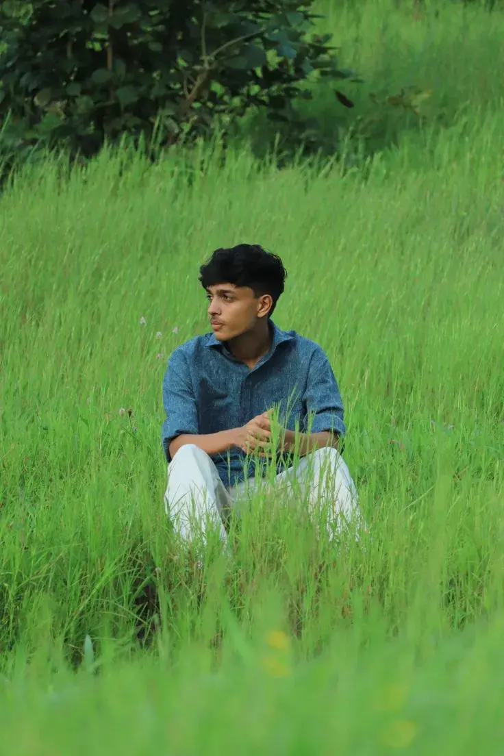 Candid Outdoor Portrait Of Young Indian Man Seated In Tall Green Grass Meadow