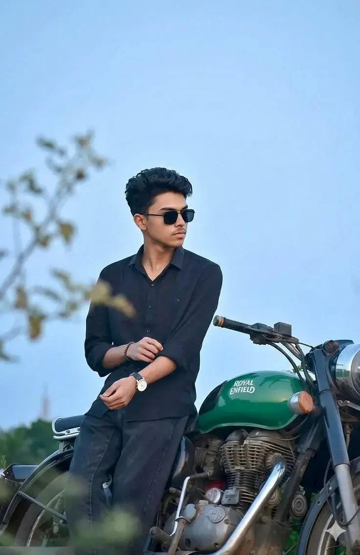 Candid Outdoor Portrait Of Young South Asian Man In Black Shirt Leaning Against Royal Enfield Motorcycle