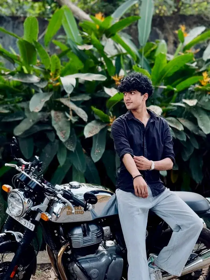 Candid Outdoor Roadside Portrait Of Young South Asian Man With Curly Hair Leaning On Chrome Royal Enfield Continental Gt
