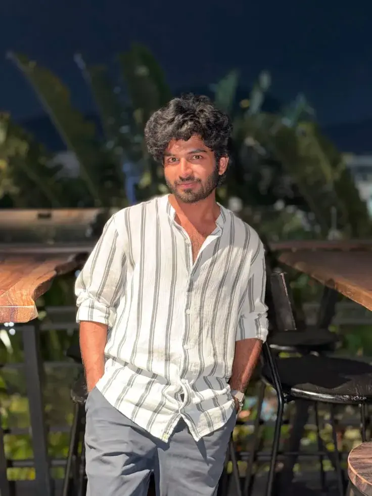 Candid Outdoor Rooftop Portrait Of Young South Asian Man In Striped Linen Shirt By Rustic Wooden Bar