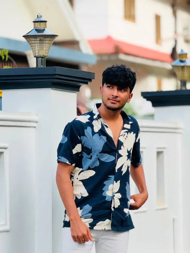 Candid Outdoor Street Portrait Of Young South Asian Man In Floral Shirt Leaning By White Boundary Wall