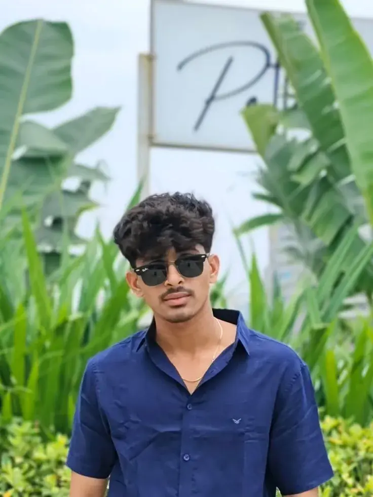 Candid Outdoor Street Portrait Of Young South Asian Man In Navy Blue Shirt And Sunglasses By Tropical Greenery
