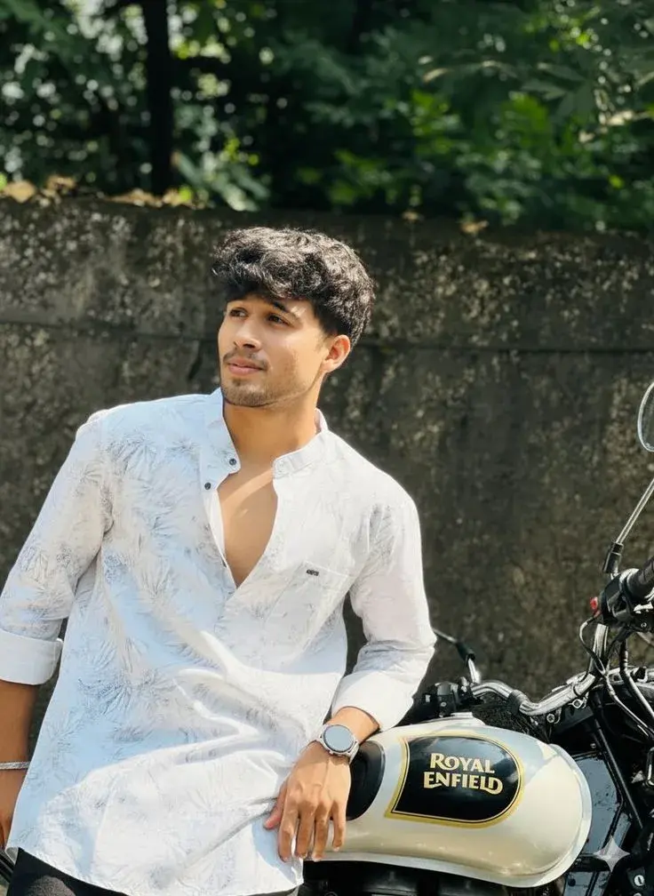 Candid Outdoor Street Portrait Of Young South Asian Man Leaning On Royal Enfield Motorcycle