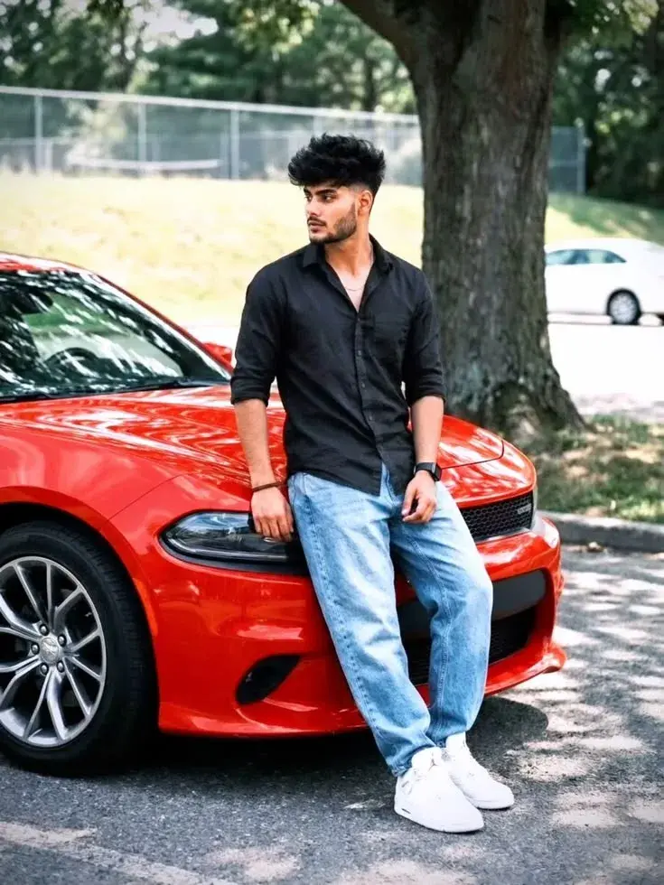 Candid Outdoor Streetwear Portrait Of Young South Asian Man Leaning On Glossy Red Muscle Car