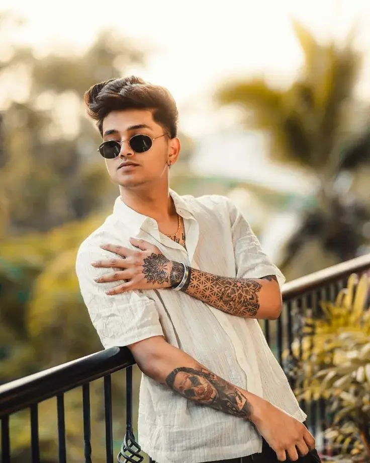 Candid Outdoor Terrace Portrait Of Young South Asian Man With Geometric Arm Tattoos Leaning On Railing