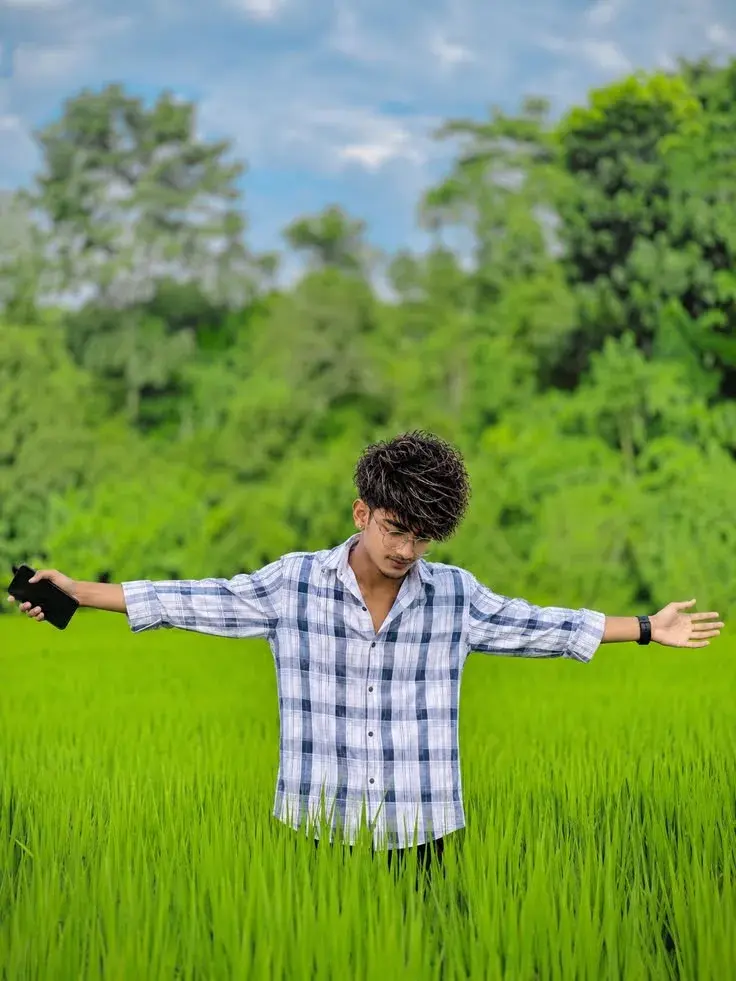 Candid Outdoor Waist-Up Portrait Of Young Indian Man With Outstretched Arms In Lush Green Field