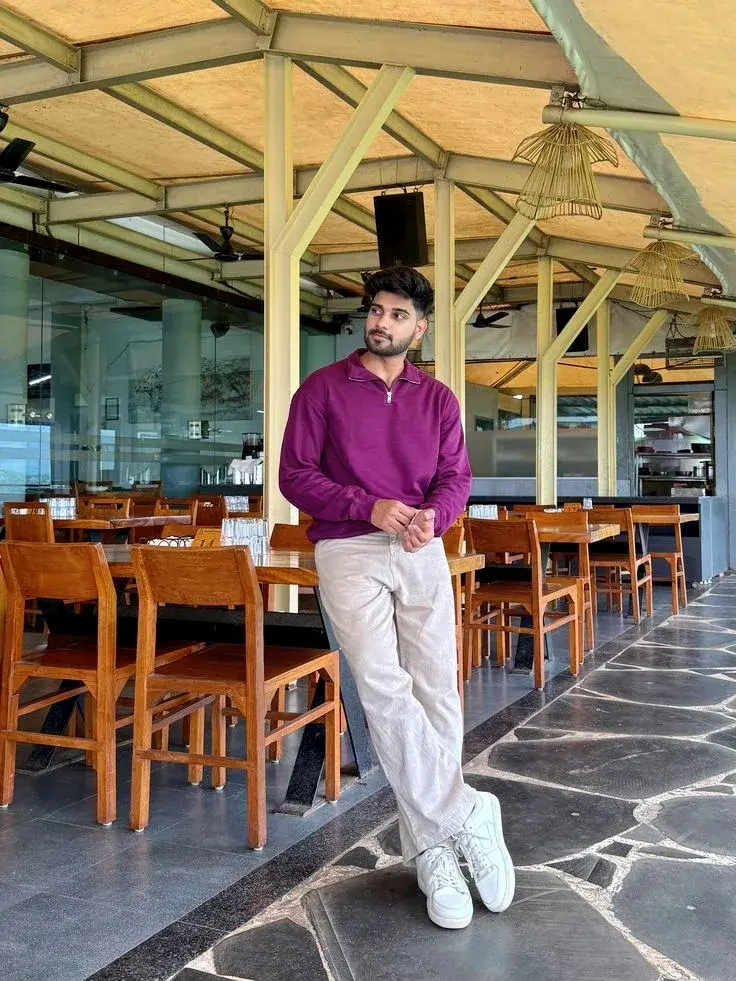 Candid Restaurant Interior Portrait Of Young South Asian Man In Magenta Quarter-Zip Pullover Leaning On Wooden Table