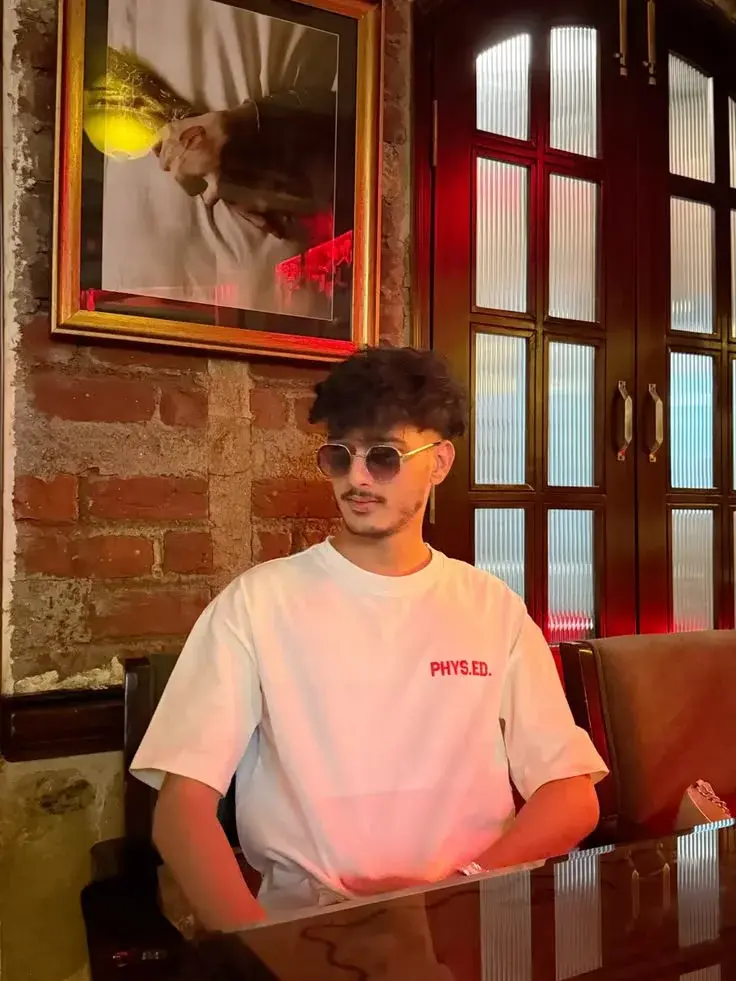 Candid Restaurant Interior Portrait Of Young South Asian Man With Textured Quiff And Sunglasses In White Graphic T-Shirt