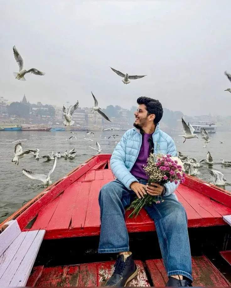 Candid Riverboat Portrait Of Smiling Young South Asian Man Holding Flower Bouquet With Flying Seagulls In Varanasi
