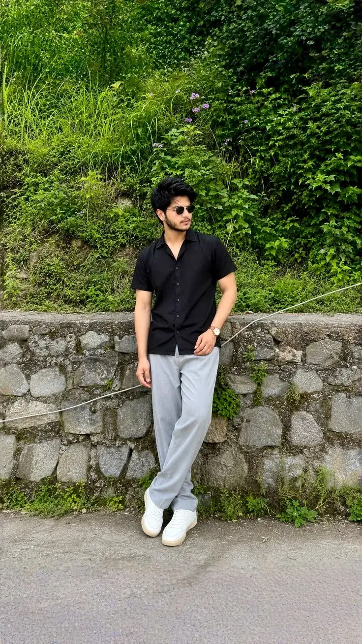 Candid Scenic Mountain Roadside Portrait Of Young South Asian Man In Black Camp Collar Shirt Leaning On Stone Retaining