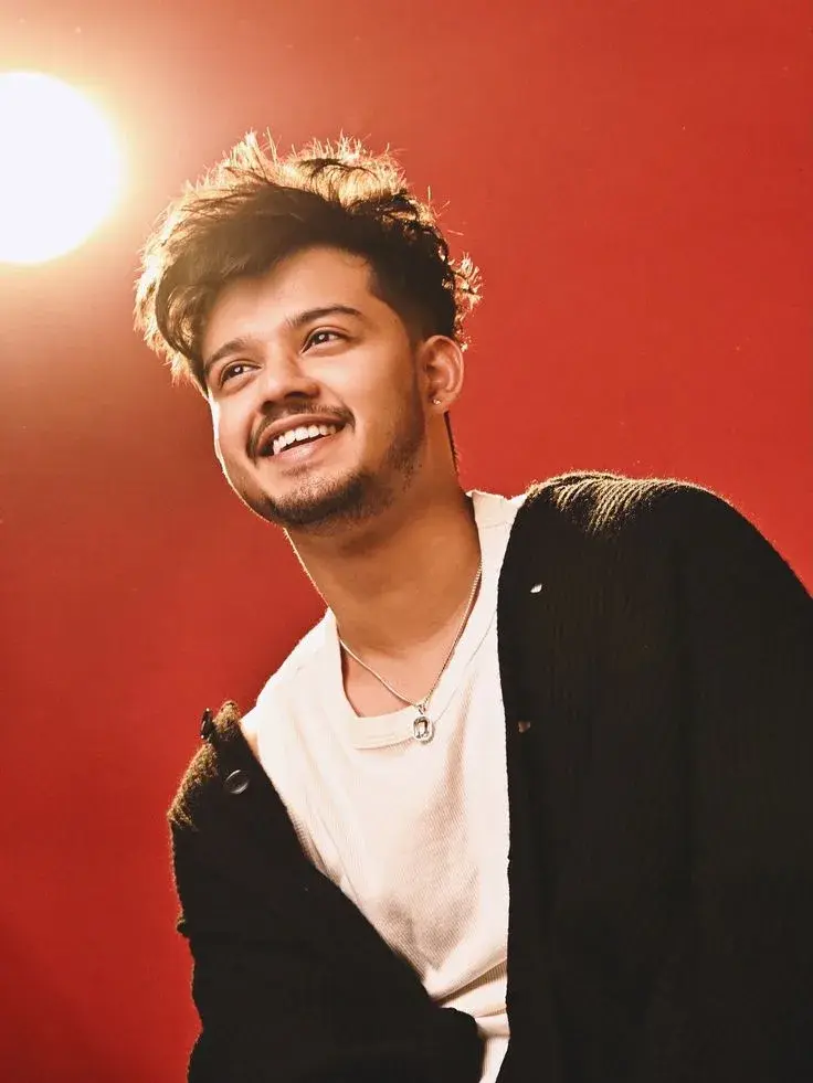 Candid Studio Portrait Of Joyful Young South Asian Man With Backlit Golden Glow On Red Background