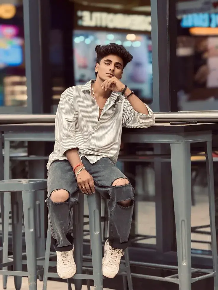 Candid Sunlit Cafe Terrace Portrait Of Stylish Young South Asian Man With Voluminous Textured Quiff Perched On High Bar