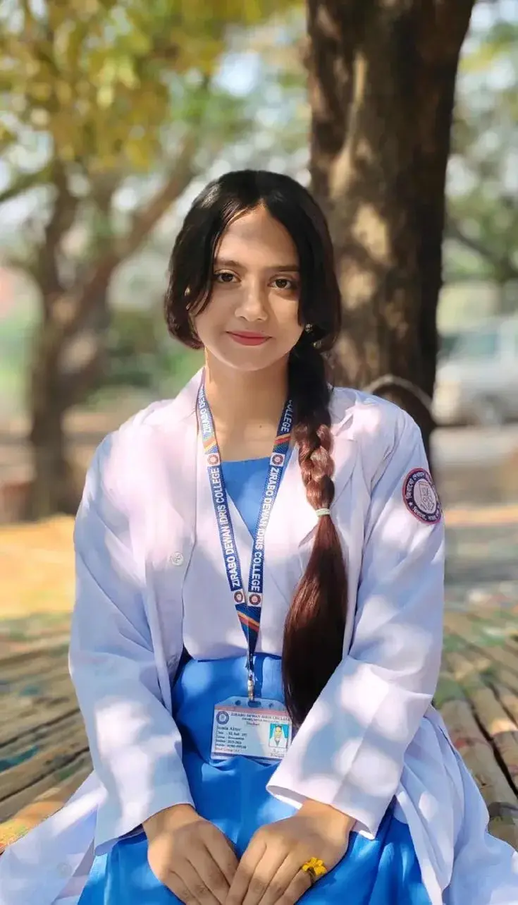 Candid Sunlit Campus Garden Portrait Of Smiling Young South Asian Student In White Lab Coat And Blue Uniform Dress With