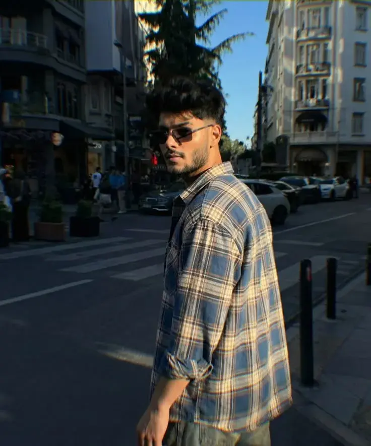 Candid Sunlit City Street Portrait Of Young South Asian Man In Blue Plaid Shirt Looking Over Shoulder With Sunglasses
