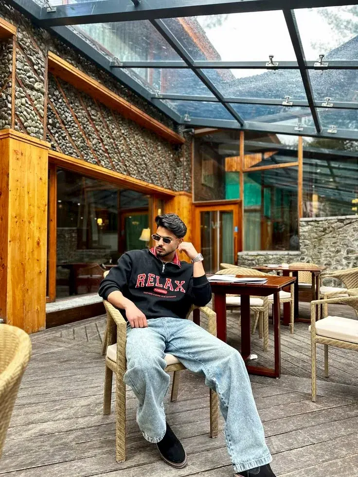 Candid Sunlit Conservatory Terrace Portrait Of Young South Asian Man In Quarter-Zip Graphic Sweatshirt Lounging On Wicke