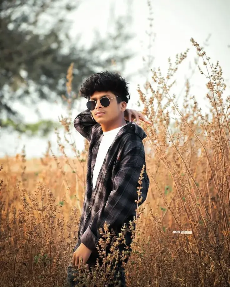 Candid Sunlit Countryside Meadow Portrait Of Young South Asian Man With Round Sunglasses And Curly Crop Hair In Plaid Sh