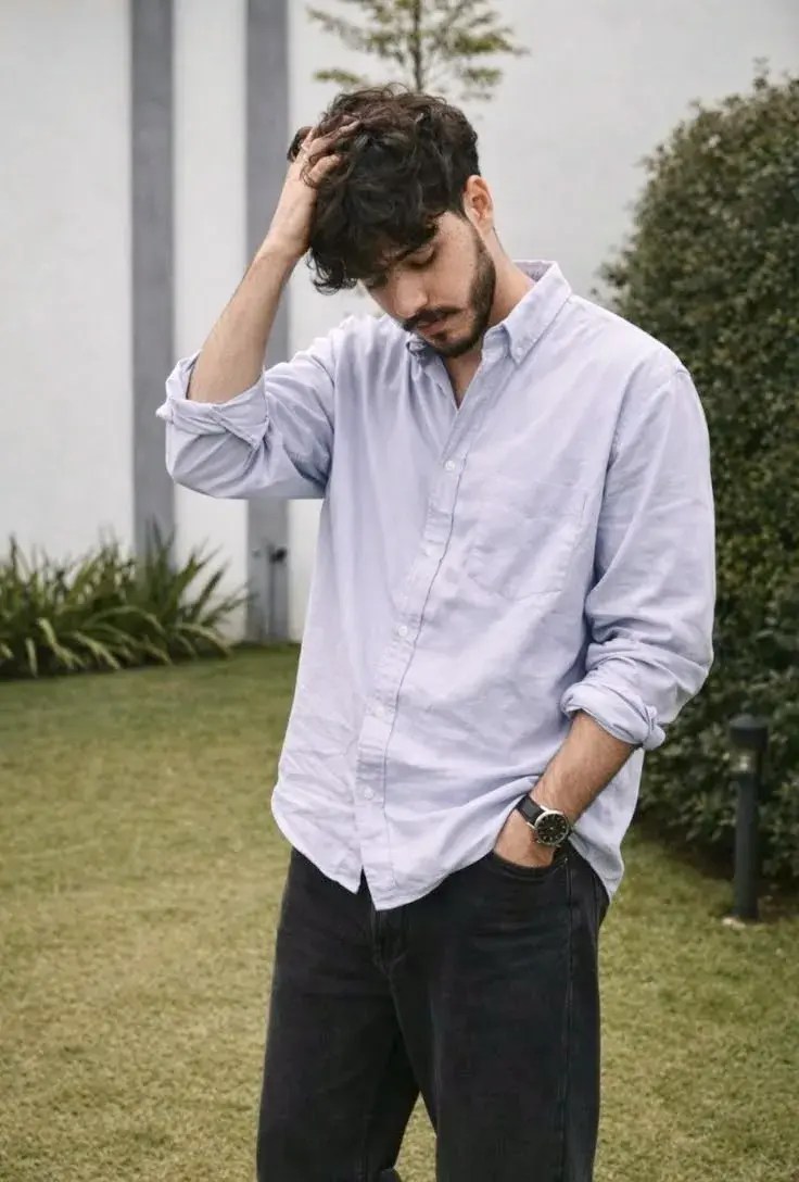 Candid Sunlit Garden Lawn Portrait Of Young South Asian Man With Hand In Tousled Wavy Hair In Light Lavender Button-Down