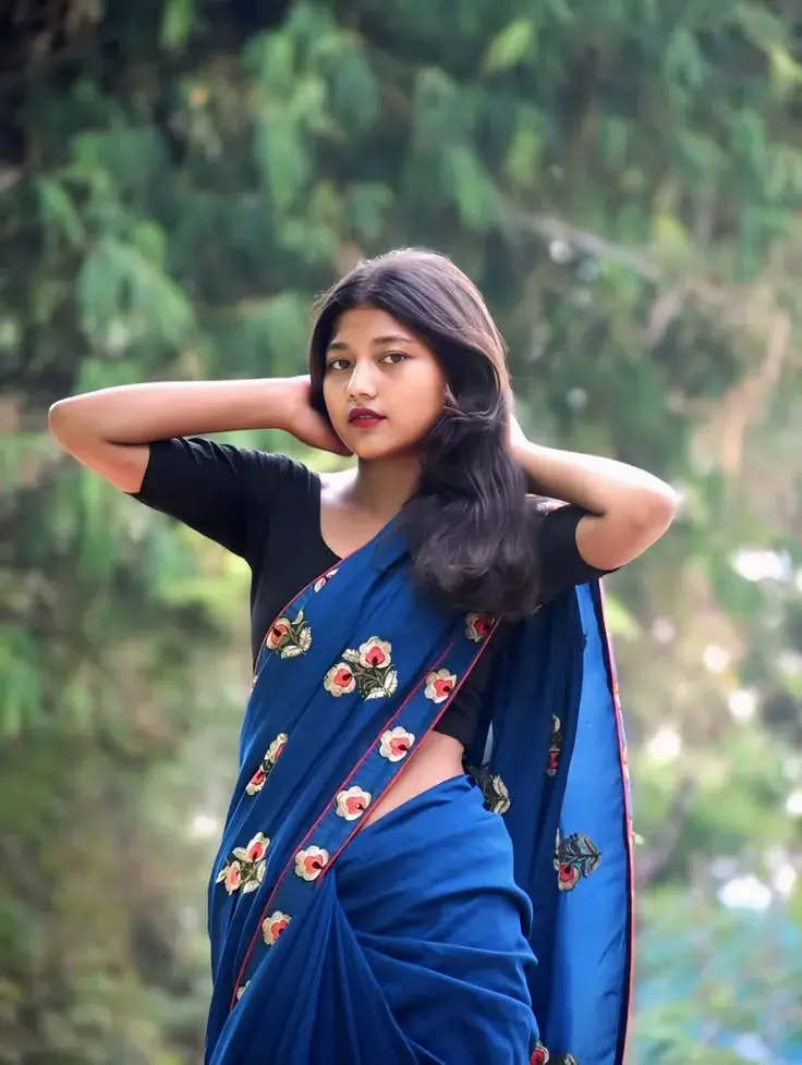 Candid Sunlit Garden Portrait Of Young South Asian Woman In Royal Blue Floral Saree With Hands Behind Hair