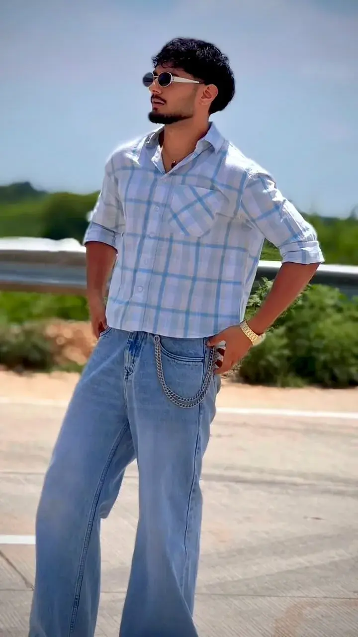 Candid Sunlit Highway Portrait Of Young South Asian Man With Oval Sunglasses In Cropped Plaid Shirt And Baggy Jeans With
