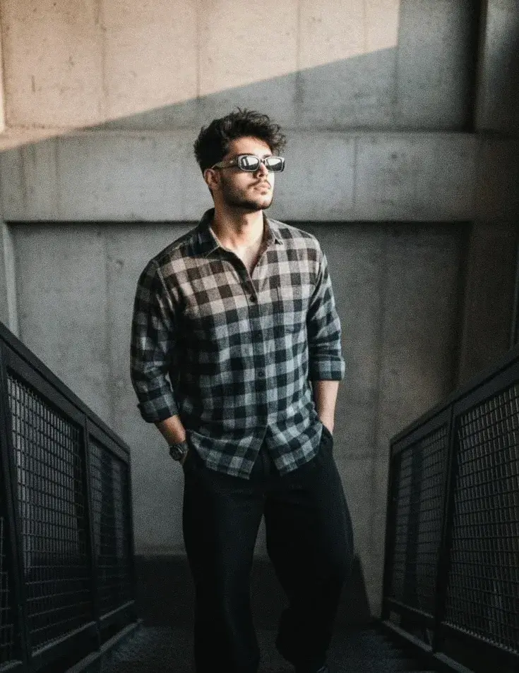 Candid Sunlit Industrial Stairwell Portrait Of Young South Asian Man With Rectangular Sunglasses In Plaid Flannel Shirt